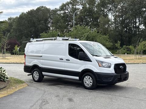 A 2023 Ford Transit van in white, featuring a black lower section and equipped with a roof rack for carrying cargo