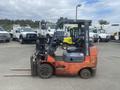 A red 2010 Toyota 7FGGU25 forklift with a black seat and lifting forks positioned on the ground