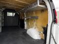 Interior of a 2014 GMC Savana van showing shelving units and a white wheel well on the right side