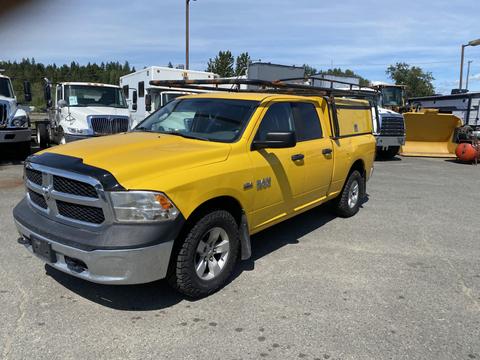 A yellow 2015 RAM 1500 pickup truck with a black grille and an attached utility cap parked with other vehicles in the background
