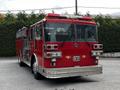 A red 1991 Sutphen Deluge fire truck with multiple emergency lights and a ladder on top stands parked, showcasing its distinctive front grille and large windows