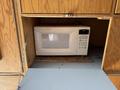A white microwave oven with a digital control panel is placed inside a wooden cabinet with an open door