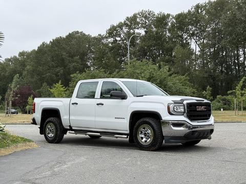 A 2016 GMC Sierra 1500 pickup truck in white with chrome accents parked, featuring four doors and large wheels