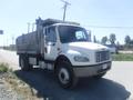 A 2005 Freightliner M2 106 Medium Duty truck with a gray dump bed and a white cab parked on the side of the road