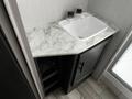 A compact bathroom sink with a white basin sits atop a marble countertop with dark cabinetry below and two glass bottles on the surface