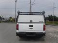 A white 2015 Chevrolet Silverado 1500 truck with a black ladder rack and a hardtop truck bed cover viewed from the rear