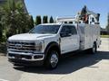 A white 2024 Ford F-550 Super Duty truck with a service body and mounted crane features chrome accents and a large front grille
