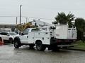 A white 2006 Ford F-450 with a bucket lift and service body parked with equipment compartments on the sides and a flatbed at the rear