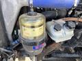 A close-up of a transparent fuel filter with a black base and a blue air intake hose connected to a Freightliner Cascadia engine الجزء.