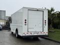 A white 2012 Ford Econoline with a large rear door and red brake lights is parked, showing its plain design and utility vehicle features