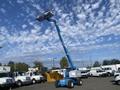 A blue 1997 Genie S-65 4X4 aerial lift with a raised platform and four large tires standing on a flat surface among vehicles