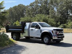 A 2019 Ford F-550 with a dump truck bed parked at an angle in a clear area surrounded by trees