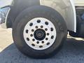 Close-up of a white steel wheel with multiple circular holes mounted on a large black tire marked Firestone and sized 2157515