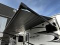 A 2021 Grand Design Reflection 311BHS recreational vehicle with a retractable awning extended over the side of the trailer