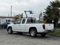 A white 2012 GMC Canyon pickup truck with a metal bed rack and chrome wheels is parked at an industrial location