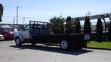 A white 2006 Ford F-650 flatbed truck with a black bed and metal railing is parked with palm trees nearby