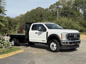 A 2023 Ford F-550 truck with a flatbed in white color parked at an angle showing its front and side profile