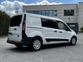 A 2016 Ford Transit Connect with a white exterior and black accents parked, featuring sliding side doors and large rear windows