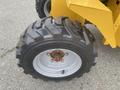A close-up of a black tire on a yellow mini loader with a sturdy tread pattern and metallic rim
