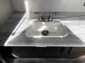 A double-handle faucet mounted over a white sink set in a light gray marble countertop