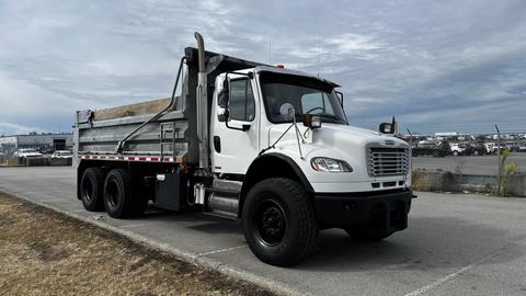 A 2010 Freightliner M2 106 dump truck with a white cab and a metallic dump bed standing on a concrete surface