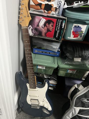 A blue electric guitar leaning against a stack of storage boxes beside a small amplifier