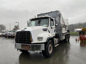A 2020 Freightliner 114SD truck with a white exterior and a large cargo container on the back parked in a rain-soaked area