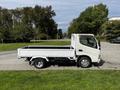 A 2004 Toyota Toyoace pickup truck in white with a flatbed design parked on a grassy area