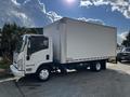 A white 2016 Isuzu NPR box truck with a large empty cargo area and a cab on the left side facing forward