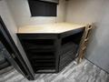 A wooden bunk bed with a ladder positioned against a dark cabinet featuring several open shelves and drawers inside a recreational vehicle