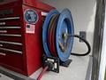A blue hose reel with red and black hoses attached, mounted next to a red tool chest adorned with a sticker that reads Make America Eat Again