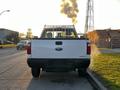 A white 2012 Ford F-250 truck with a metal bed rack parked on the street facing away with smoke rising in the background