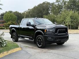 A black 2024 RAM 2500 truck with a tall stance aggressive front grille and large off-road tires parked on a paved surface