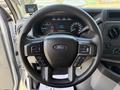 Steering wheel of a 2023 Ford E-450 featuring audio controls and a central Ford logo with various instrument panel displays visible behind it