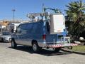 A blue 2008 Ford E-350 van equipped with a ladder rack and utility box on the roof and a rear step bumper with reflective tape