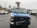 A 2009 Ford Econoline with a blue front, black grille, and an elevated work platform on top, featuring strapping across the grille for support