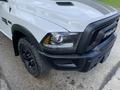 A 2021 RAM 1500 in white with a black grill and hood stripes features angular headlights and a rugged tire design