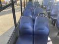 A row of blue upholstered bus seats with a simple design and armrests visible in a transit vehicle interior