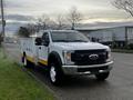 A 2019 Ford F-550 truck with a white and yellow exterior featuring a utility bed and front orange beacon lights