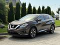 A 2016 Nissan Murano in a brown color parked with its headlights on and sleek body lines showcasing its modern design and alloy wheels
