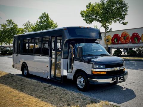 A 2019 Chevrolet Express bus with a black front and silver side featuring large windows and an open door