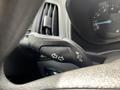 An interior view of a 2016 Ford Transit Connect's turn signal lever positioned on the steering column with illuminated indicators on the dashboard behind it