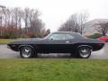A 1974 Dodge Challenger in black with chrome wheels parked on a wet surface showcasing its classic muscle car design and sleek profile