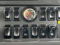 A control panel with multiple black switches and a circular air pressure gauge displaying 100 PSI in the center