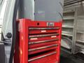 A red tool chest with multiple drawers labeled Beach positioned next to a white vehicle's side door
