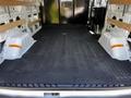 Interior of a 2023 Ford Transit van featuring a rubber mat and wooden shelving along the sides with a metal partition at the back