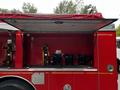 A red 1991 Sutphen Deluge fire truck with an open storage compartment revealing black equipment mounts inside