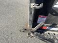 A close-up of the latch mechanism of a 2024 Southland 18 Foot Dump Trailer showing the metal components and warning label attached to the trailer