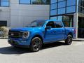A blue 2021 Ford F-150 truck with a sleek design and black wheels parked in front of a modern building