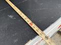 A wooden measuring tape extended across a black surface marking measurements in inches with a visible measurement of 28 inches